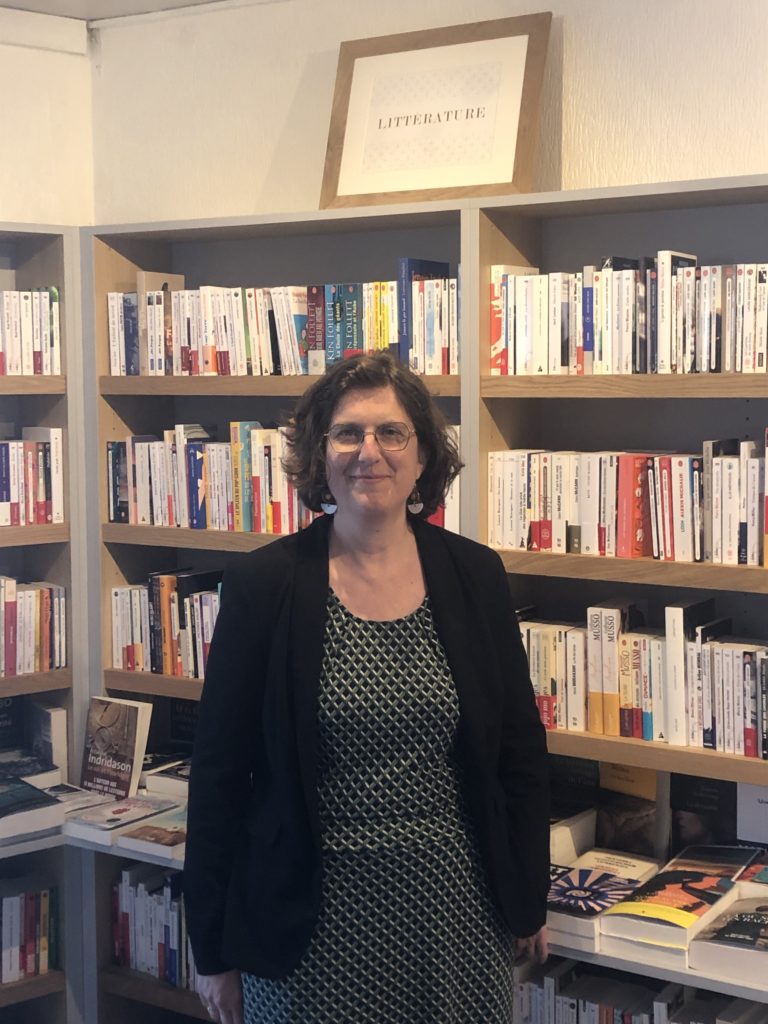 Photo de la libraire, Hélène Martineau, devant le rayon littérature de la librairie.